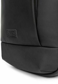 Black backpack made of smooth material, featuring a rounded shape, a textured zipper, and a rectangular logo patch on the front.