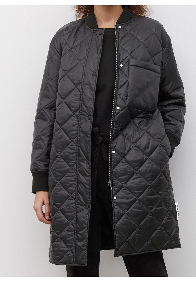 Sort quiltet lang frakke med trykknaplukning, lynlåsåbning foran, sidelommer og ribbet kant. Glat, skinnende ydermateriale.