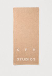 Beige tørklæde lavet af blødt stof. Har en subtil tekstur med trykt hvid tekst, der lyder "CPH STUDIOS" langs den nederste kant.