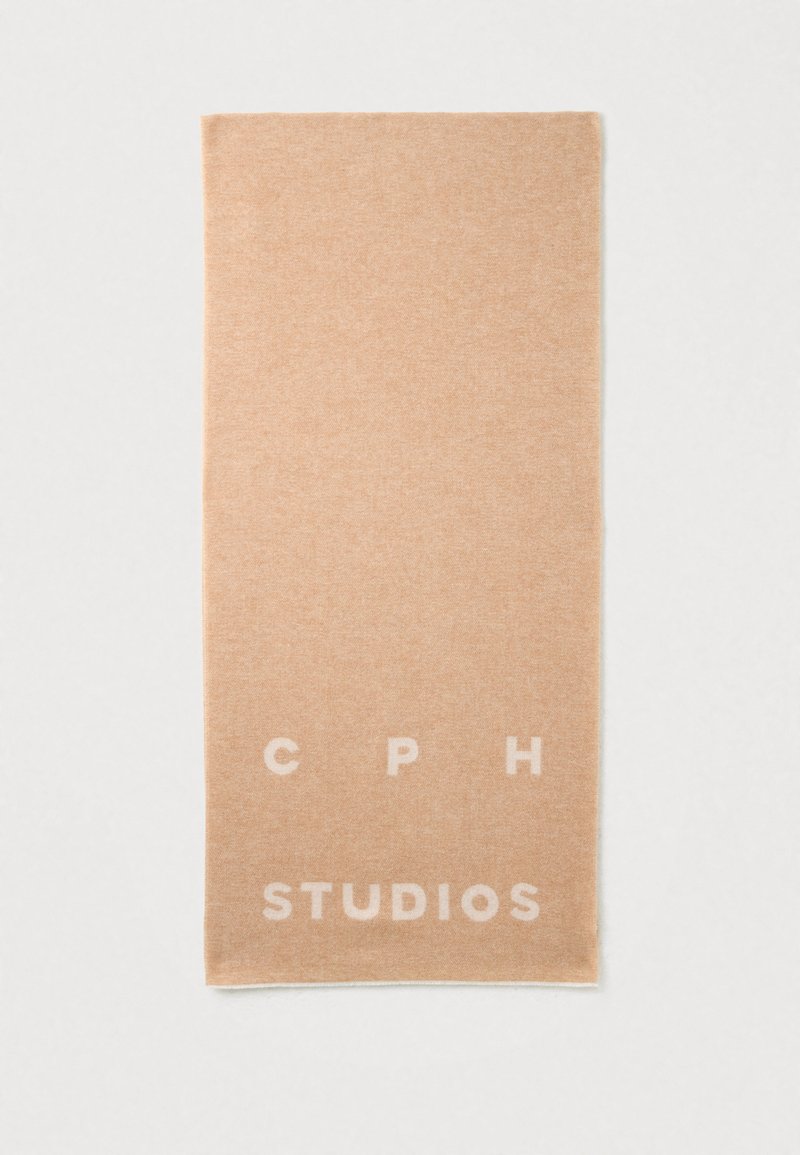 Beige tørklæde lavet af blødt stof. Har en subtil tekstur med trykt hvid tekst, der lyder "CPH STUDIOS" langs den nederste kant.