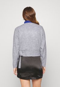 Grå stickad kappa med en knytning i midjan, tillsammans med en minikjol i svart satin. Har långa ärmar och en rundad halsringning.