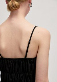 Zwarte jurk met dunne bandjes en een geplooid ontwerp. Soepele textuur zichtbaar op de stof. Eenvoudig rugdetail met verstelbare bandhardware.