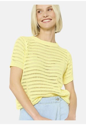 Pull en tricot jaune à manches courtes, doté d'un design ouvert et respirant, avec une coupe décontractée, associé à un jean bleu clair.