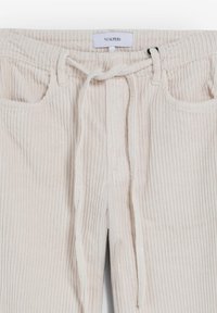 Pantalones de pana de color beige claro con cinturilla elástica, cierre de cordón y dos bolsillos frontales. Patrón acanalado texturizado en toda la prenda.