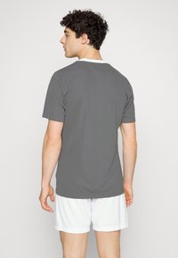 Camiseta gris de manga corta con cuello redondo, textura suave y corte regular, combinada con pantalones cortos blancos. Se muestra la vista trasera.