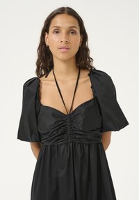 Sort kjole lavet af satin, med en samlet bust, korte puf�ærmer og en flydende nederdel. Tynde bindebånd ved halsudskæringen fremhæver designet.