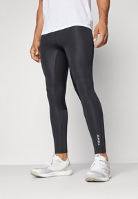 Leggings negros hechos de una tela elástica, con un diseño ajustado que presenta paneles laterales en contraste y un logo 'TECHFIT' en la parte inferior de la pierna.