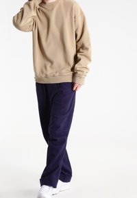 Beige oversized mikina s kulatým výstřihem, doplněná volnými námořnickymi kalhotami a bílými teniskami. Viditelná měkká textura látky.
