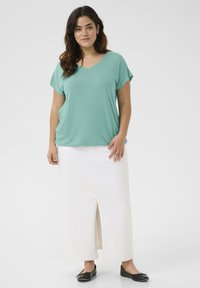 Mint green V-neck shirt with short sleeves, paired with a white, knee-length skirt featuring a front slit, worn with black flats.