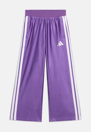 Pantaloni sportivi largi mov cu dungi albe pe lateral, talie elastică, buzunare și un logo alb Adidas pe coapsa dreaptă.