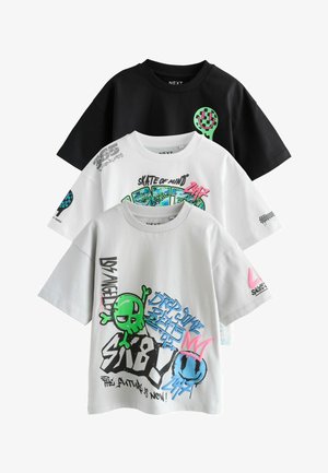 Tre grafiske t-shirts: sort med et grønt smilende ansigt, hvid med farverig alien og tekst, grå med farverigt sprawl-print. Bomuldsstof, afslappet pasform.