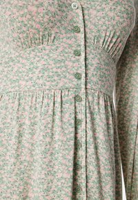 Vestito verde con motivo floreale caratterizzato da piccoli fiori rosa, texture a coste, chiusura con bottoni e vita arricciata per uno scopo sagomante.