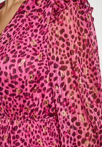 Rotes Kleid aus einem transparenten, strukturierten Stoff mit einem Leopardenmuster. Rüschenärmel und goldene Akzente vervollständigen das Design.