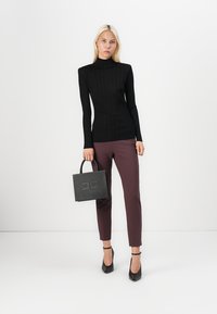 Suéter de gola alta canelado preto, design justo; calças slim-fit bordeaux; pequena mala preta com detalhes de tachas; saltos pretos.