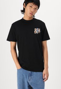 Schwarzes Baumwoll-T-Shirt mit einem bunten Grafikdruck auf der linken Brust. Klassische Passform mit rundem Hals und kurzen Ärmeln.