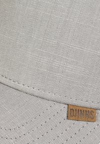 Gorra de tela gris con un acabado texturizado. Presenta una etiqueta de logo de cuero marrón, detalles cosidos y un diseño de visera curvada.