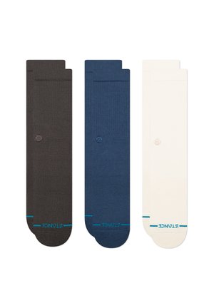 Drie paar sokken: donkerbruin, marineblauw en crème. Elk paar heeft een gladgebreide textuur en een klein logo op het bovenste gedeelte.