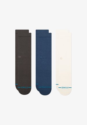 Drei Paar Socken: dunkelbraun, marineblau und cremefarben. Jede verfügt über eine glatte Strickstruktur und ein kleines Logo im oberen Bereich.