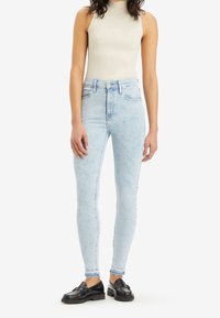 Jeans skinny azzurri chiari con vita alta e sfumature delicate. Abbinati a un top a coste beige e mocassini neri.