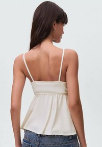 Lys beige peplum-top med tynde stropper og en samlet talje, lavet af et blødt, struktureret stof. Ingen synlige mønstre eller detaljer.
