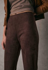 Braune Wildlederhosen mit glatter Textur und einer figurschmeichelnden Silhouette, mit hoher Taille und einem sauberen, nahtlosen Design.