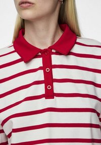 Camisa polo a rayas rojas y blancas con cuello rojo sólido. Presenta una tapeta de tres botones y una textura de tela suave.