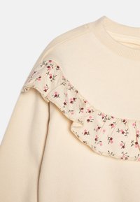 Krémová mikina s nabíraným límcem a květinovým vzorem v růžové a hnědé barvě. Měkká textilie a žebrovaný detail kolem krku.