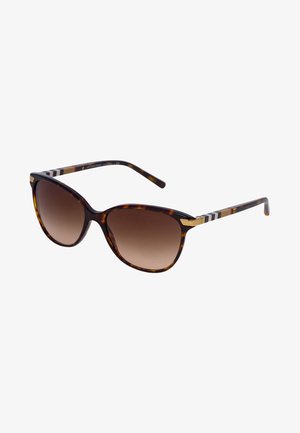 Óculos de sol em tartaruga com lentes castanhas em degradê. Forma de olho de gato, acentuados com um design de hastes listradas em preto e dourado.