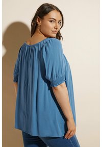 Blå, lös passform blus med korta, elastiska puffärmar och en rynkad halsringning; slät textur och en avslappnad silhuett.