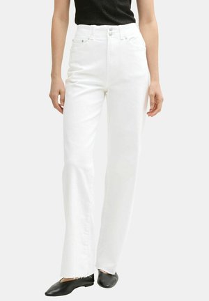 Witte high-waisted jeans met een rechte pijp, voorzien van voorzakken en een rafelrand, gecombineerd met zwarte platte schoenen en een zwart topje.