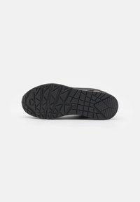 Black rubber shoe sole with a textured pattern featuring deep treads and ridges for grip. Flat design, rounded toe, and reinforcement details.