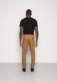 Chinos tan con un corte slim y bolsillos traseros. Combinados con una camiseta negra de cuello redondo y zapatos negros. Diseño minimalista, textura suave.