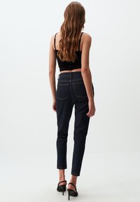 Jeans in denim scuro con vestibilità slim, dotati di tasche posteriori, cuciture a contrasto e spacchi laterali alla caviglia, abbinati a un top corto nero e tacchi.