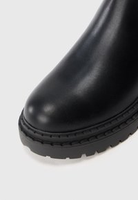 Stivale in pelle nera con punta arrotondata e suola in gomma spessa e texture su sfondo bianco.