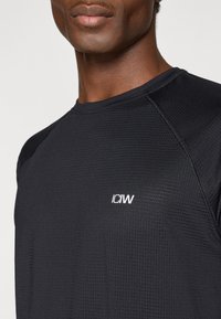 Μαύρο αθλητικό μπλουζάκι με υφή υφάσματος, με ραγλάν μανίκια και μικρό λευκό λογότυπο "ICIW" στο στήθος.