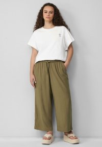 Weißes Baumwoll-T-Shirt mit kurzen Ärmeln, das mit einem kleinen floralen Stickmuster verziert ist. Olivgrüne, weite Hosen mit elastischem Bund.