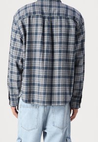 Camisa de franela a cuadros en azul y gris, con cuello clásico y mangas largas, con un dobladillo ligeramente curvado y puños con botones.