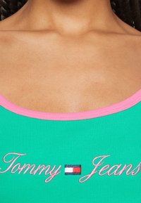 Top tank verde a righe con rifinitura rosa, caratterizzato da testo ricamato "Tommy Jeans" e un piccolo dettaglio con la bandierina del logo.
