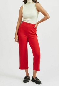 Rode, halflange broek met een elastische tailleband, gemaakt van glad, rekbaar materiaal. Gecombineerd met een aansluitende, mouwloze crèmekleurige coltrui.