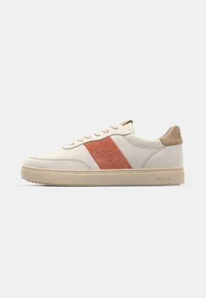 Vita sneakers med en röd perforerad sidpanel och beige detaljer. Har en rund tå, platta snören och en strukturerad gummisula.