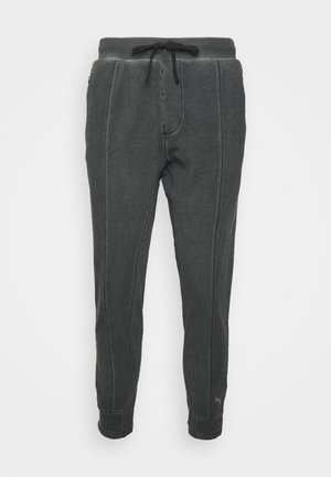 Donkergrijze taps toelopende joggingbroek met zichtbare naden, een elastische tailleband en een zwart trekkoord.