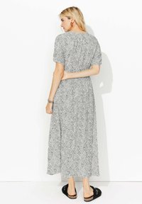 Robe midi à motifs noir et blanc avec des manches courtes et un dos froncé, présentant une silhouette fluide et portée avec des sandales noires à enfiler.