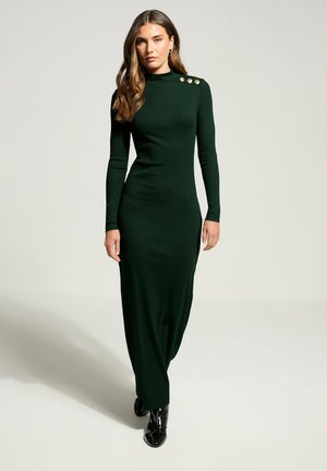 Abito a maglia a coste verde scuro con collo alto, maniche lunghe e dettagli in bottoni dorati sulle spalle. Silhouette lungo il pavimento con una vestibilità affusolata.