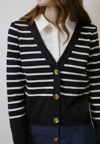 Marineblauwe en witte gestreepte cardigan met een V-hals, met gouden knopen aan de voorkant. Ribstof met een getailleerde pasvorm.