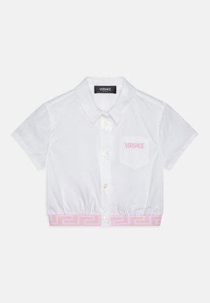Hvit kortermet skjorte med krage og innsvingt midje, med et rosa gresk nøkkelmønster nederst og en lomme med "Versace"-logo.