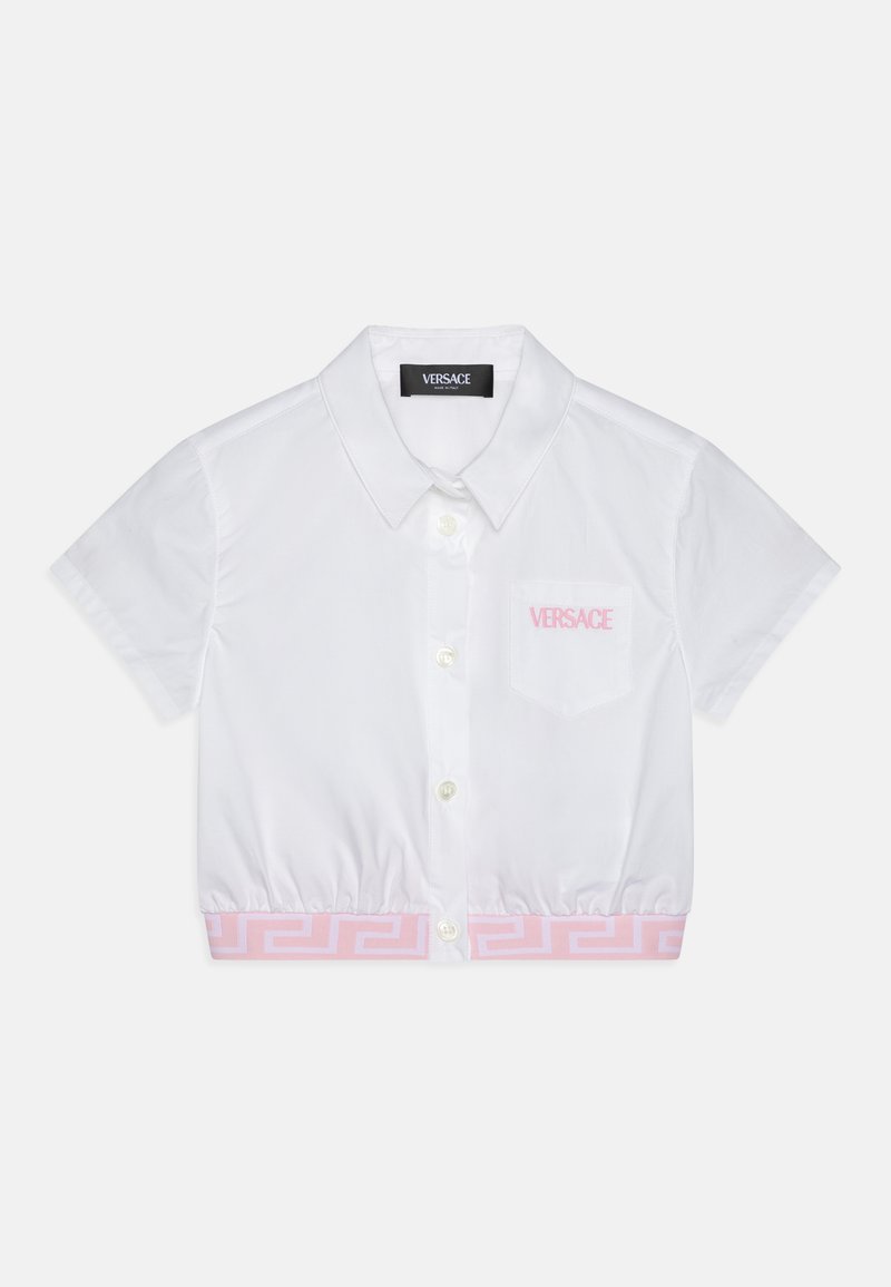 Hvit kortermet skjorte med krage og innsvingt midje, med et rosa gresk nøkkelmønster nederst og en lomme med "Versace"-logo.