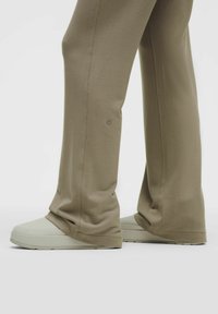 Beige színű, laza fazonú melegítők, puha anyagból készítve. Kicsi logó található a boka magasságában. Világos színű sportcipőkkel párosítva.