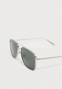 Gafas de sol con montura de metal plateado, lentes tintadas en gris y detalles texturizados en las patillas. Diseño geométrico definido. Fabricadas en Japón.
