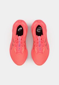 Helle pinkfarbene Sportschuhe mit einem textilen Obermaterial, flachen Schnürsenkeln und einer gepolsterten Sohle. Verfügt über ein Logo auf der Zunge und gemusterte Akzente an den Seiten.