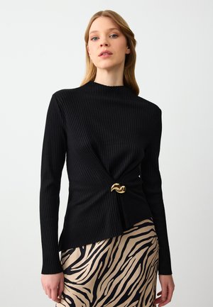 Top lungo a maniche, nero, a coste, con collo alto e dettaglio frontale attorcigliato caratterizzato da un'accensione in hardware color oro. Abbinato a una gonna a fantasia.